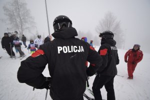 Policjanci na nartach stojący tyłem w tle narciarze